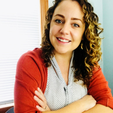 Woman smiling, wearing red sweater, curly hair.