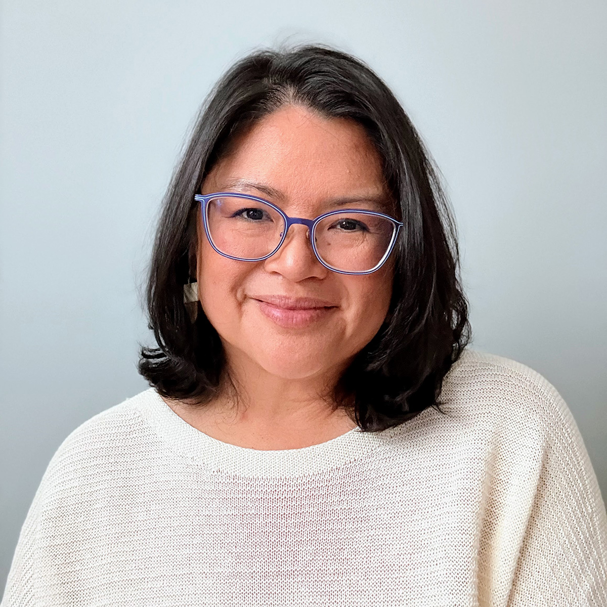 Smiling person wearing glasses and white sweater.